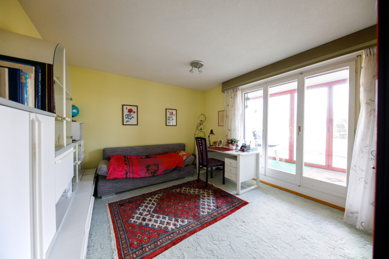 Helles Zimmer mit Sofa, Schreibtisch und Balkonzugang
