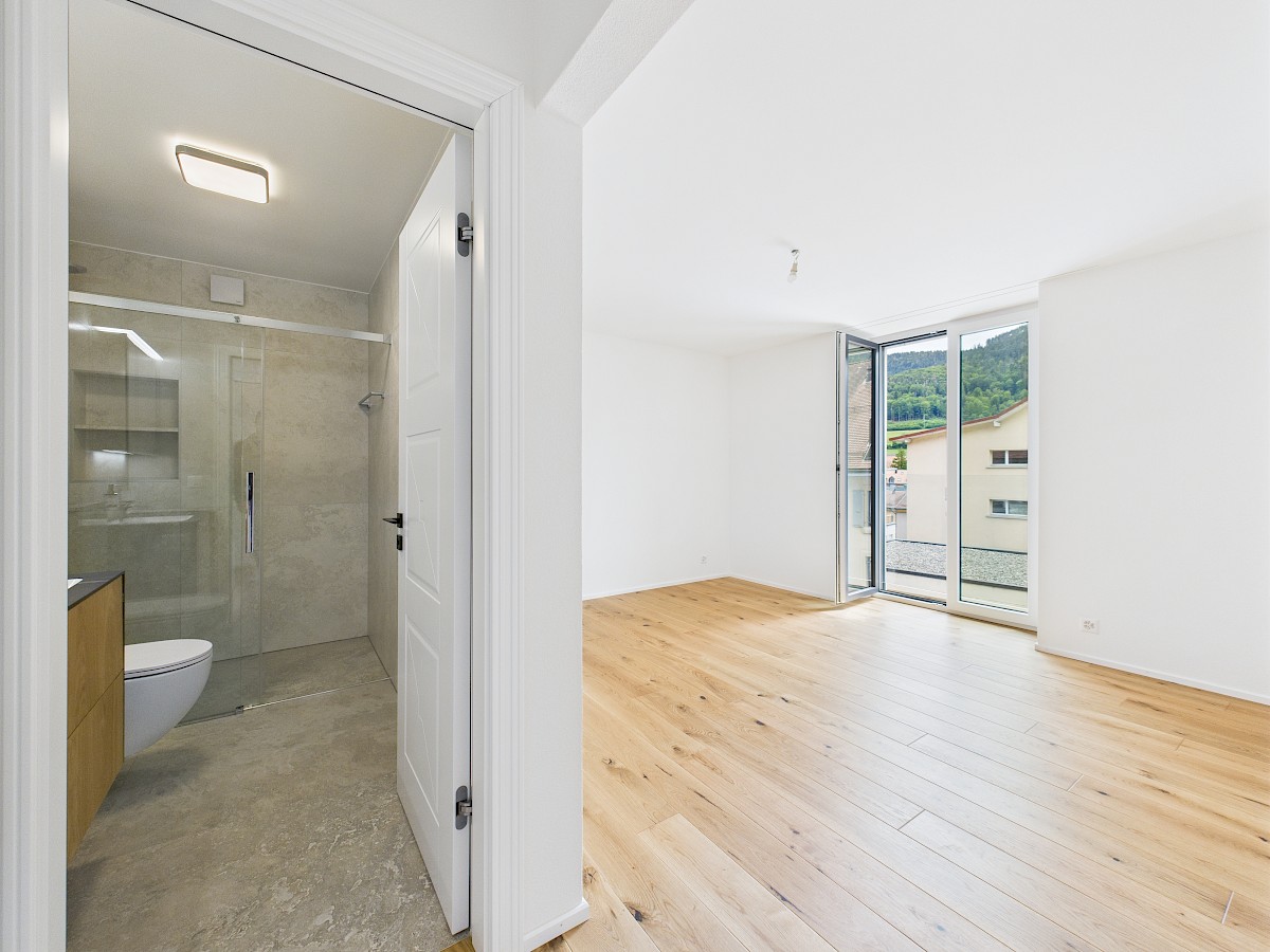 Helles Badezimmer neben leerem Wohnraum mit Balkonblick