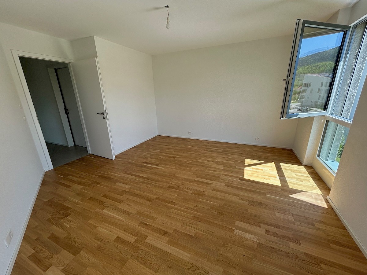 Heller, leerer Wohnraum mit Parkett und großem Fenster