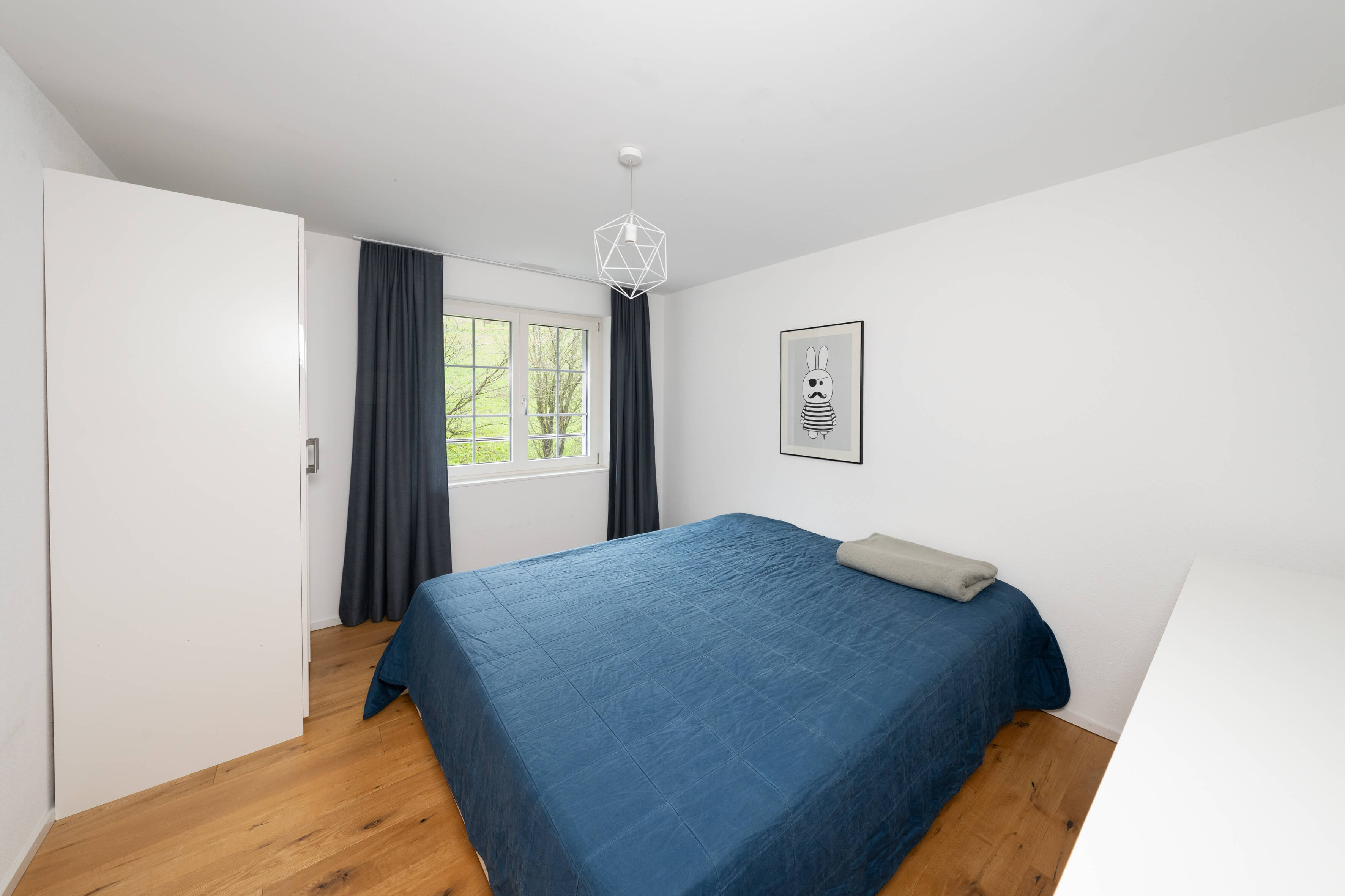 Helles Schlafzimmer mit blauem Bett und weißen Wänden