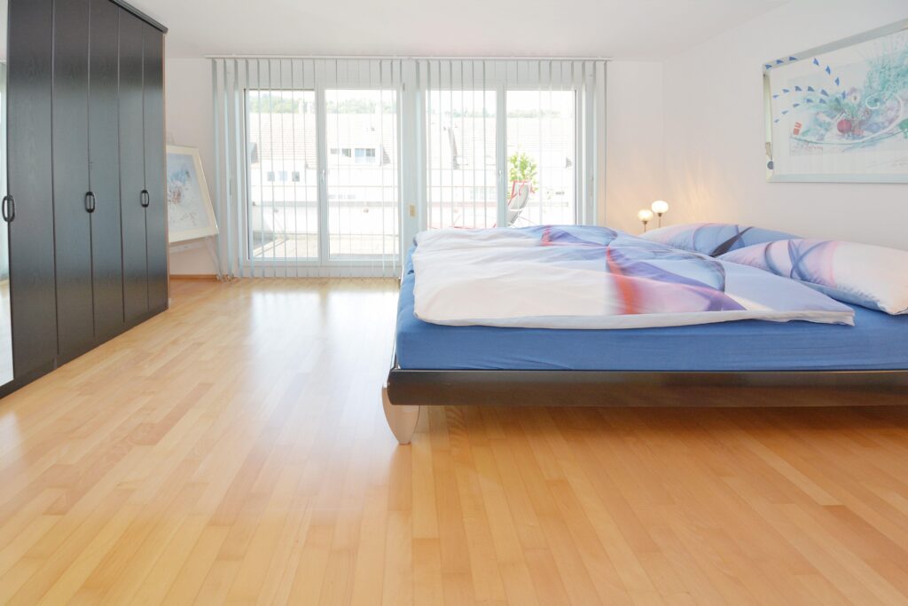 Helles Schlafzimmer mit großem Fenster und dunklem Kleiderschrank