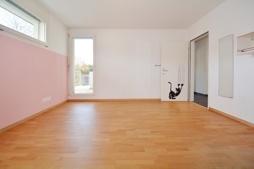 Helles, leeres Zimmer mit Parkett und rosafarbener Akzentwand