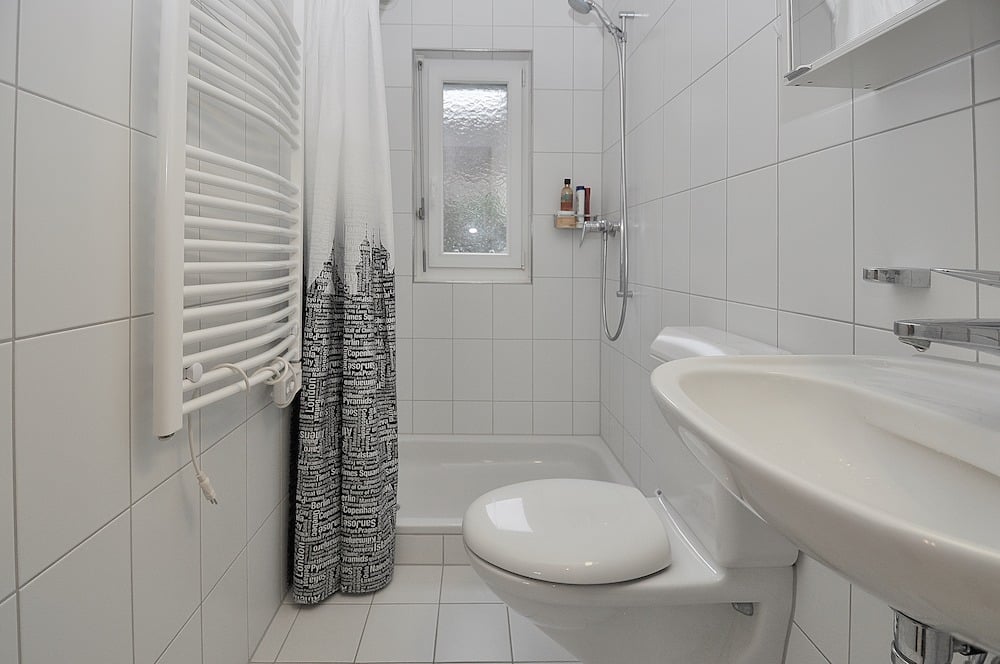 Helles, schmal geschnittenes Badezimmer mit Dusche, WC und Waschbecken