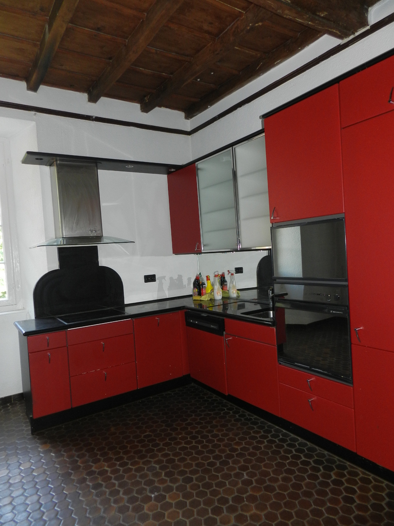 Rote Küche mit dunklem Holzbalkendecken und hexagonalem Boden