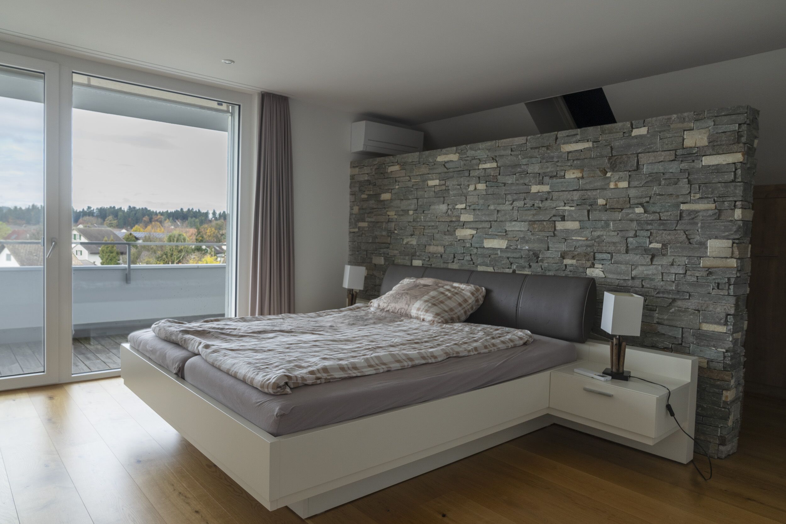 Modernes Schlafzimmer mit Balkon und Naturstein-Akzentwand