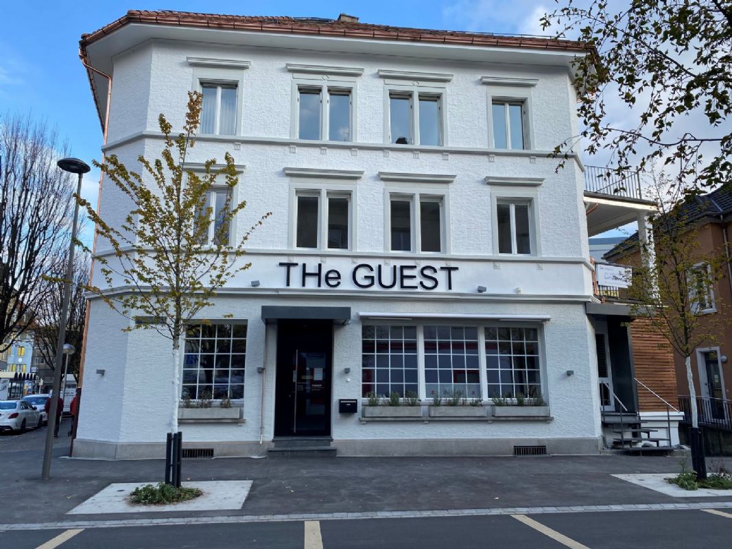 Mehrfamilienhaus mit Gewerbeanteil und Schild 'The GUEST'