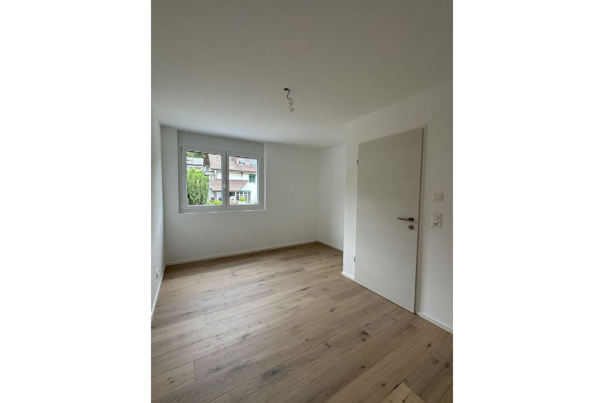 Helles, leeres Zimmer mit Parkettboden und Fenster