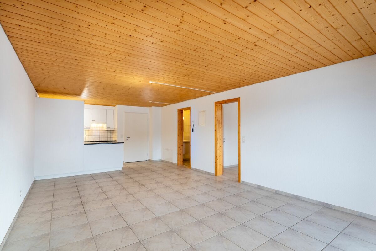 Heller, leerer Wohnraum mit Holzdecke und Küchenzeile