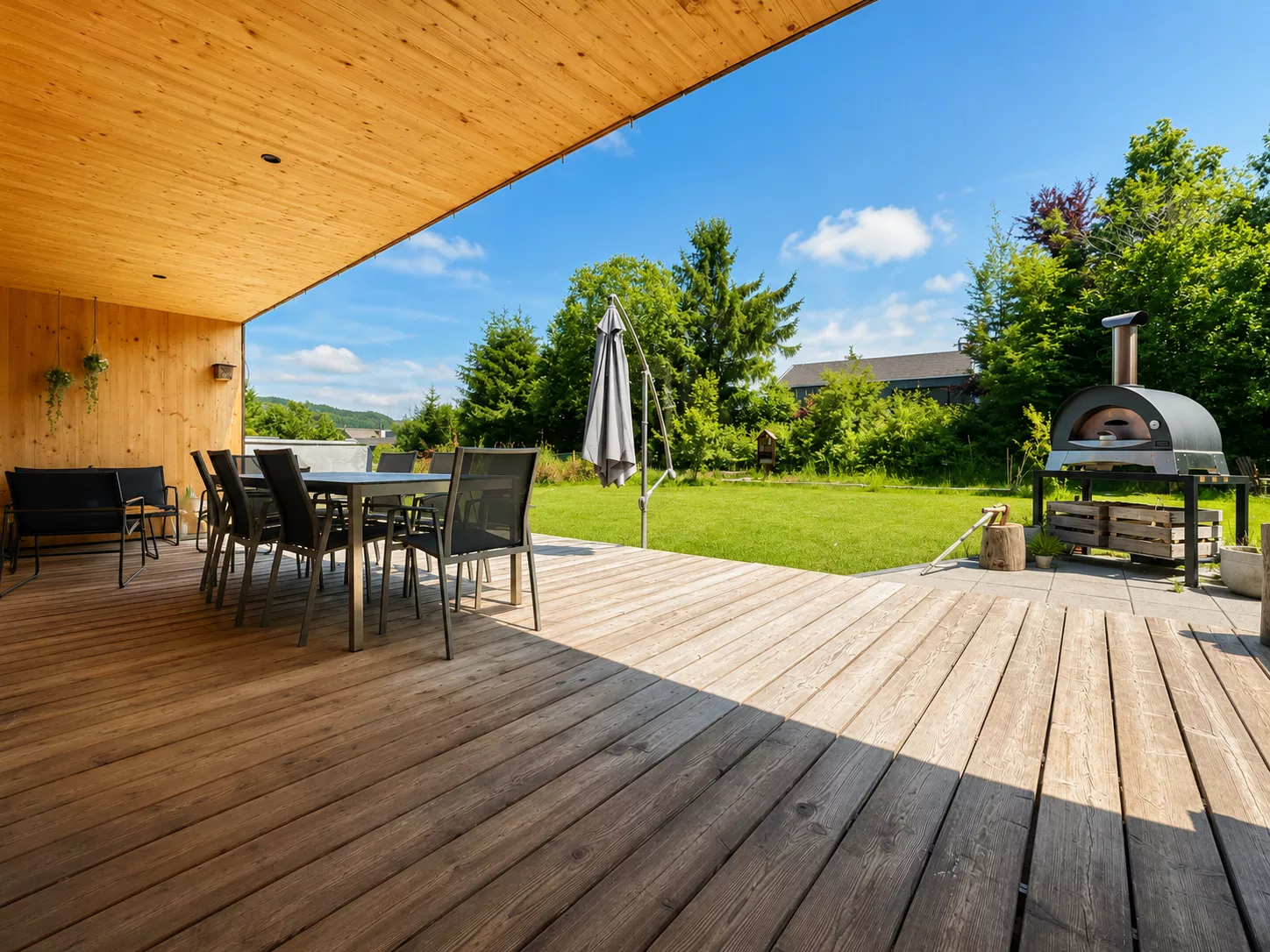 Überdachte Holzterrasse mit Garten und Pizzaofen