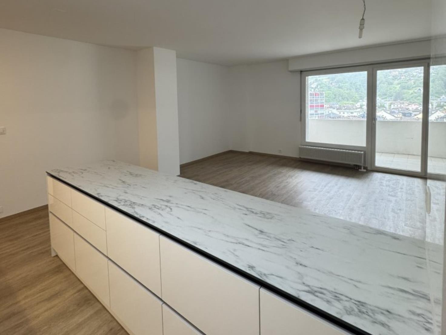 Offener Wohnbereich mit Kücheninsel und Balkonblick