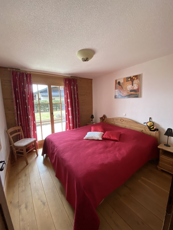 Schlafzimmer mit Holzfensterfront und roter Tagesdecke