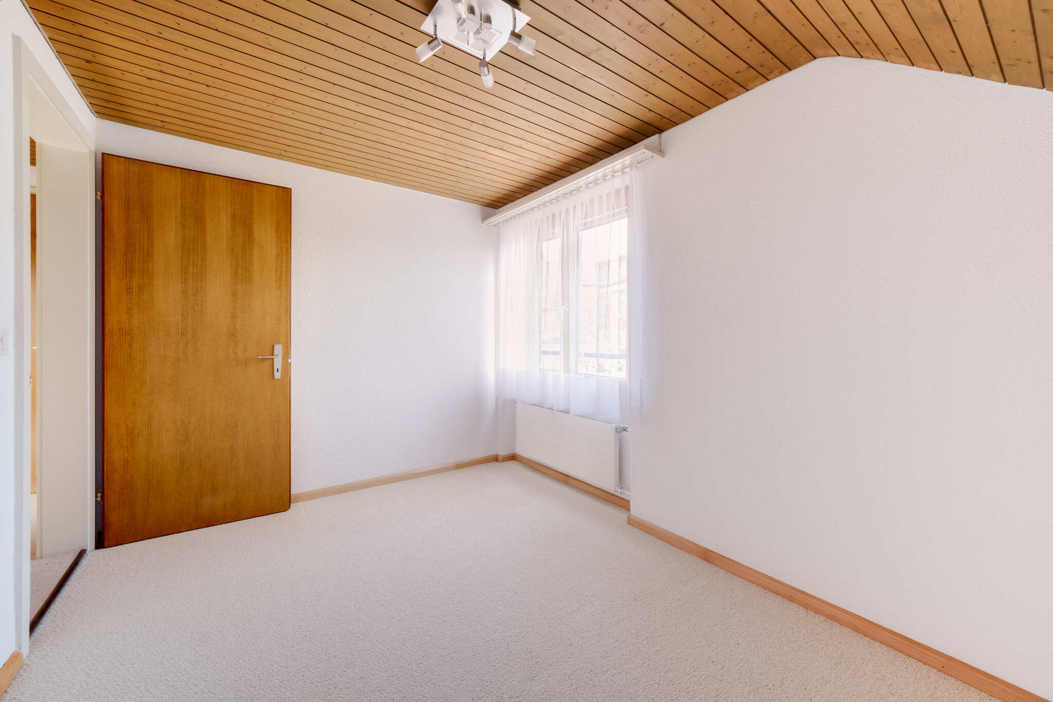 Helles, schlichtes Zimmer mit Holztür und Dachholzdecke