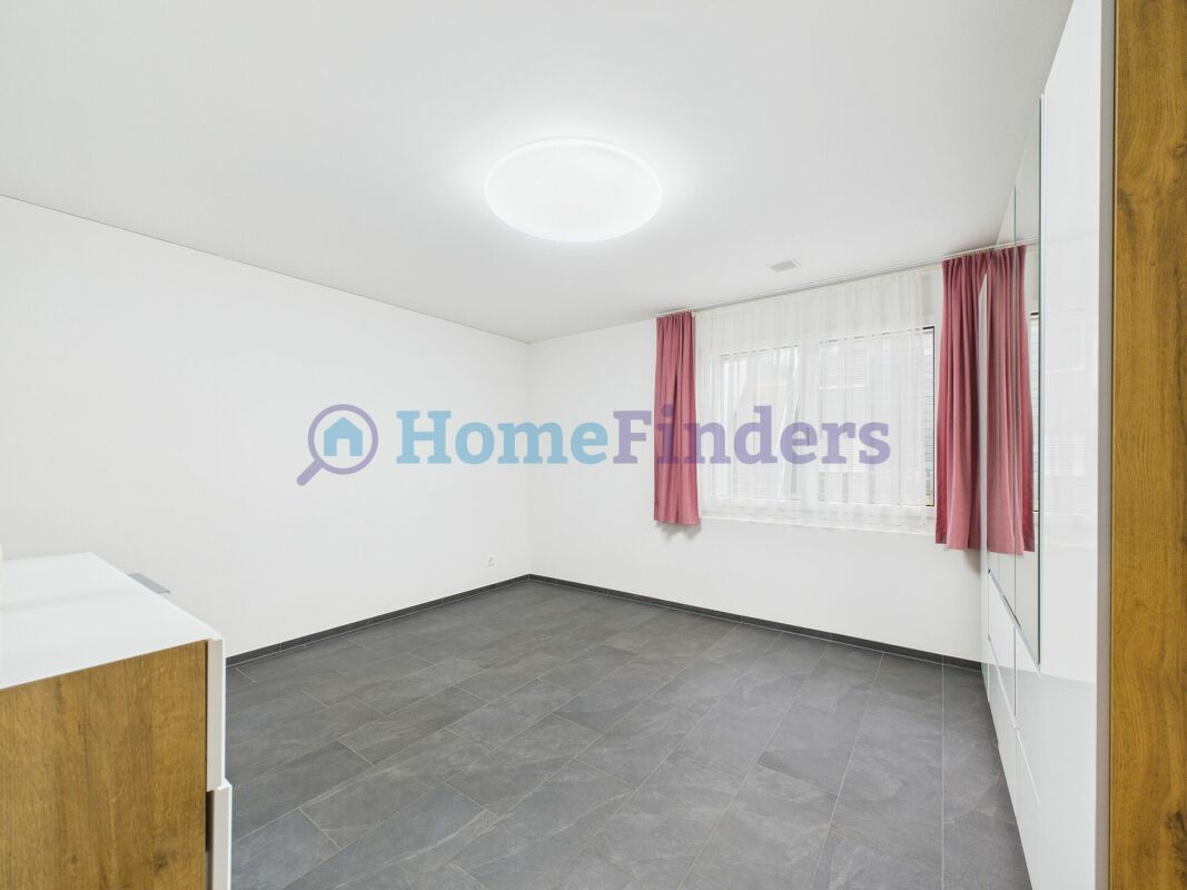 Helles, leeres Schlafzimmer mit grauem Fliesenboden und Fenster mit rosa Vorhängen.