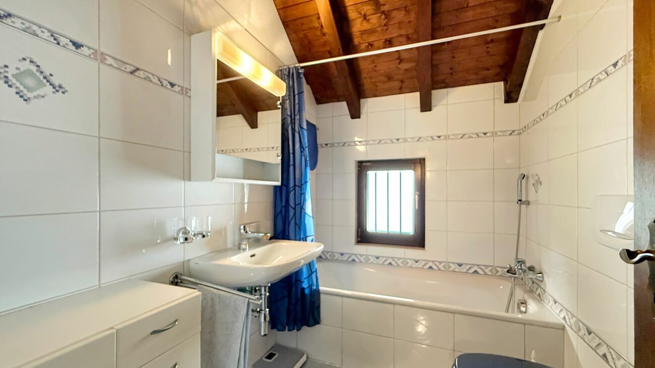 Badezimmer mit Badewanne und Holzbalkendecke