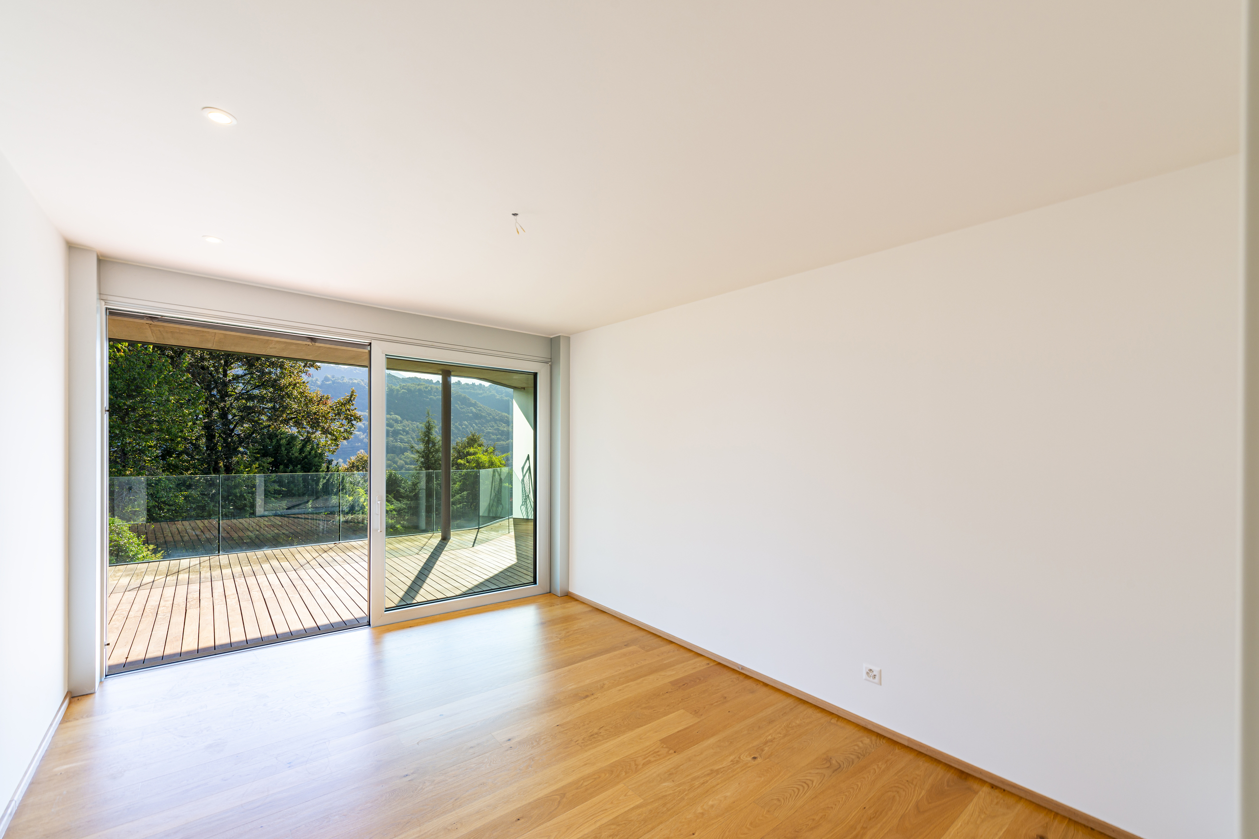 Heller leerer Raum mit Holzfußboden und großer Schiebetür zum Balkon