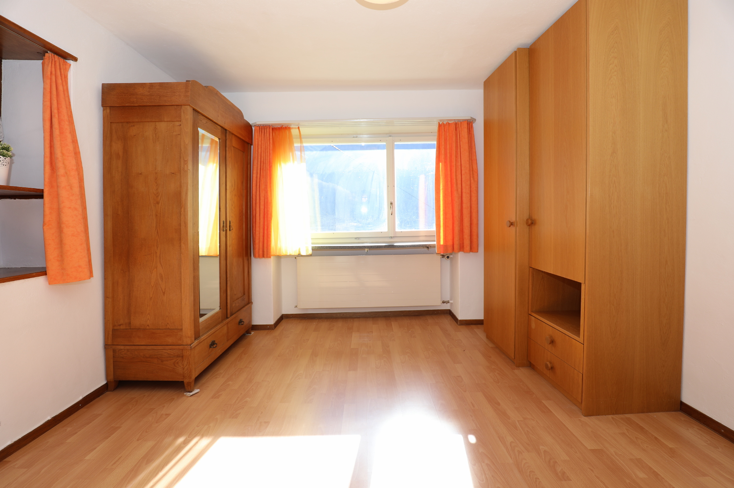 Schlafzimmer mit Holzschränken und orangefarbenen Vorhängen