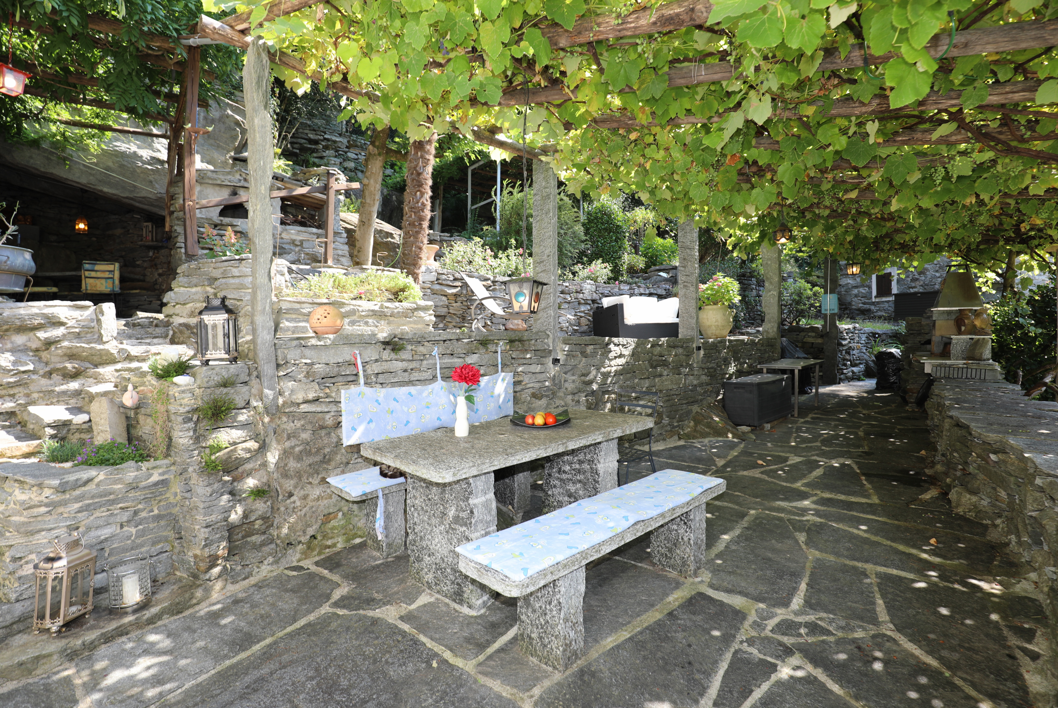 Steinverkleideter Außen-Sitzbereich unter Weinpergola