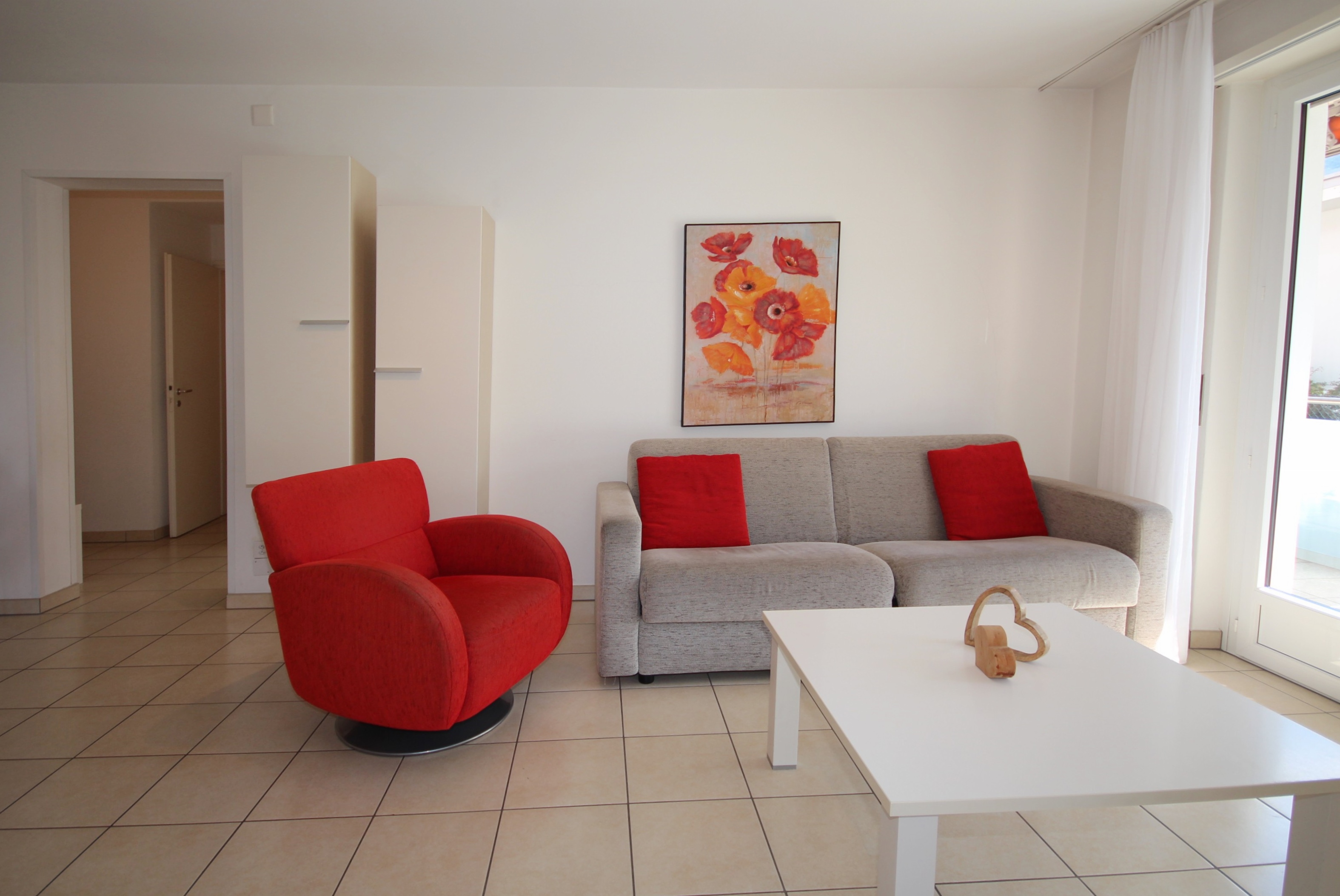 Helles Wohnzimmer mit rotem Sessel und Sofa
