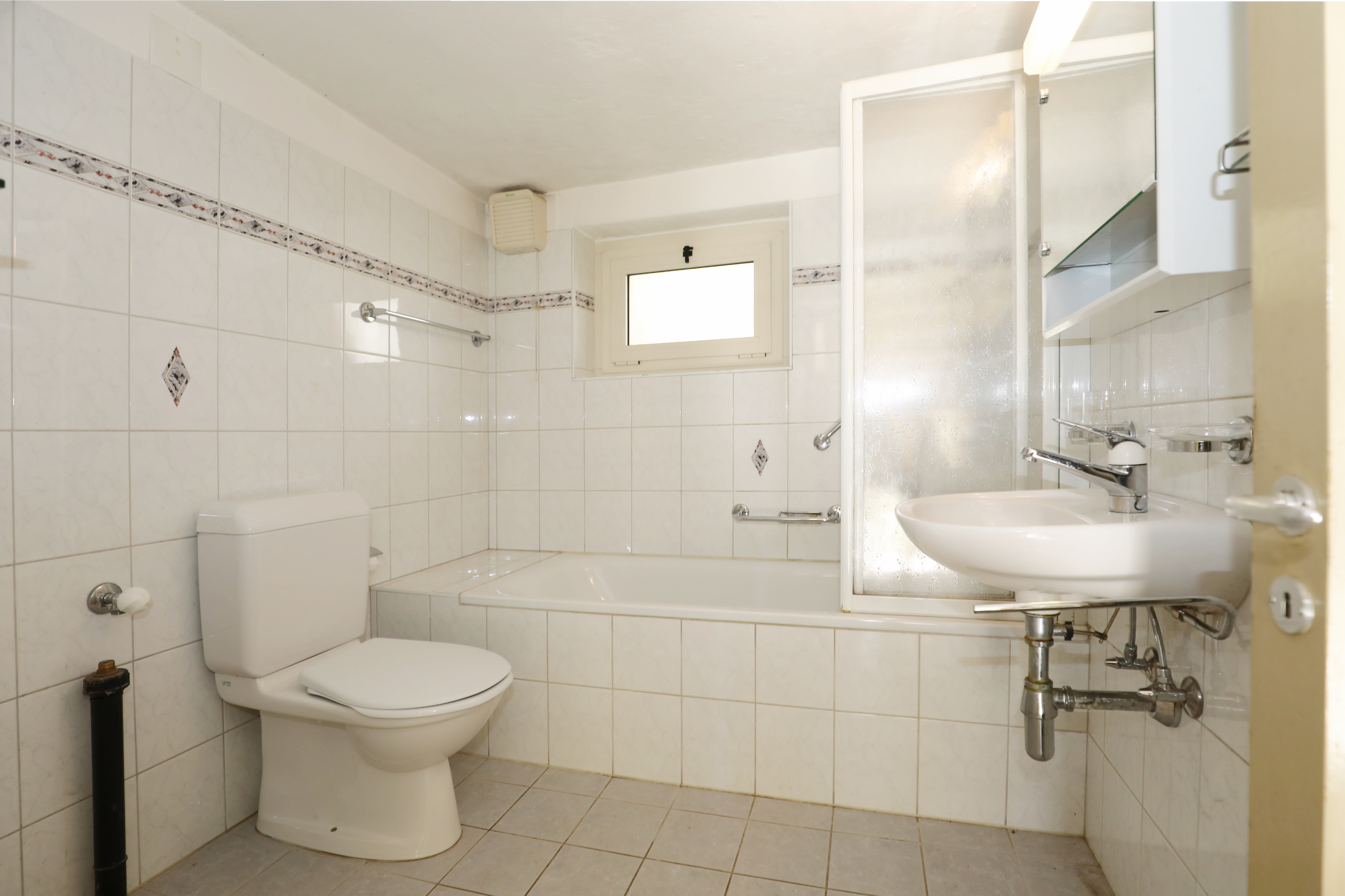 Kleines weiß gefliestes Badezimmer mit Badewanne, WC und Waschbecken
