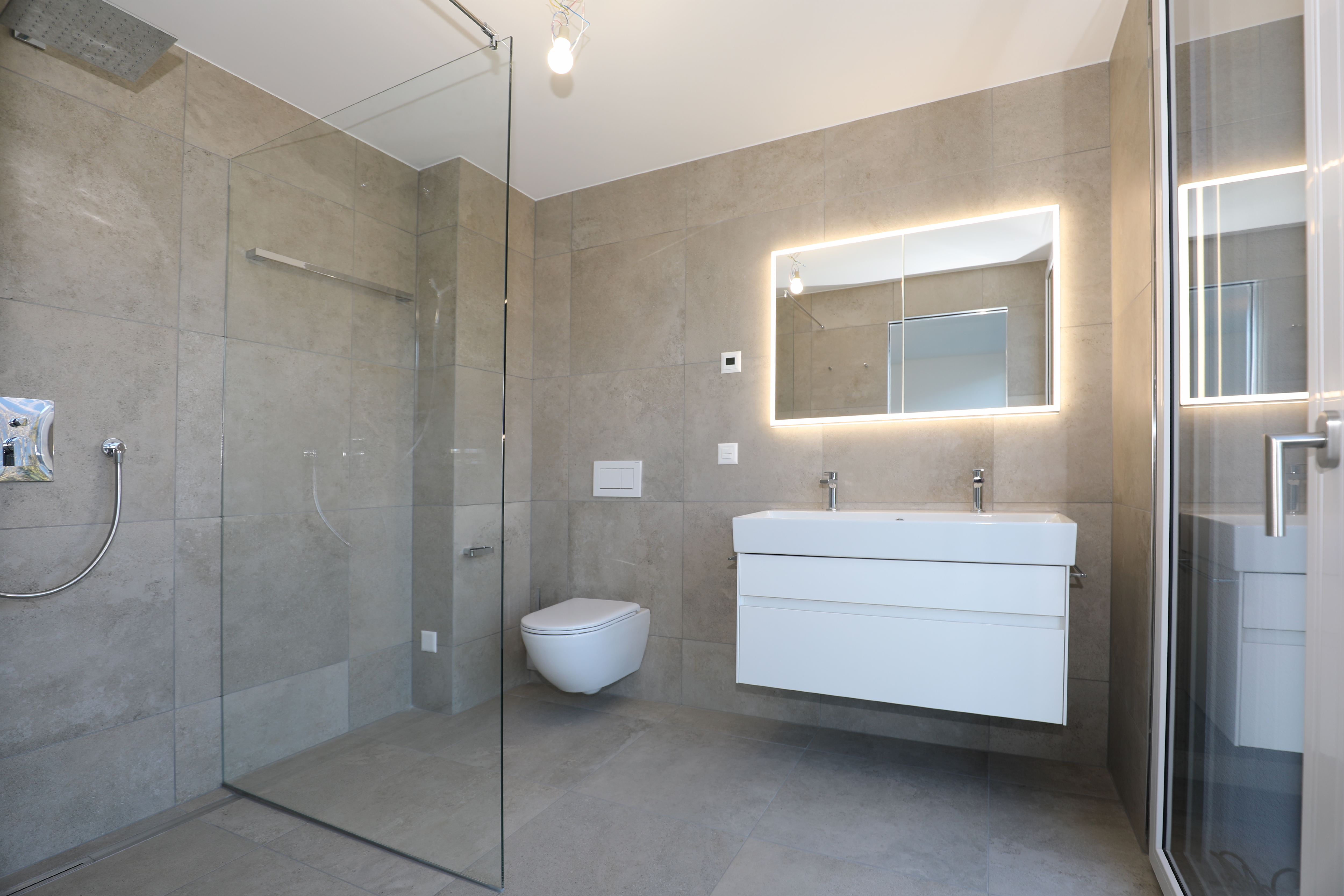 Modernes Badezimmer mit begehbarer Dusche und beleuchtetem Spiegel