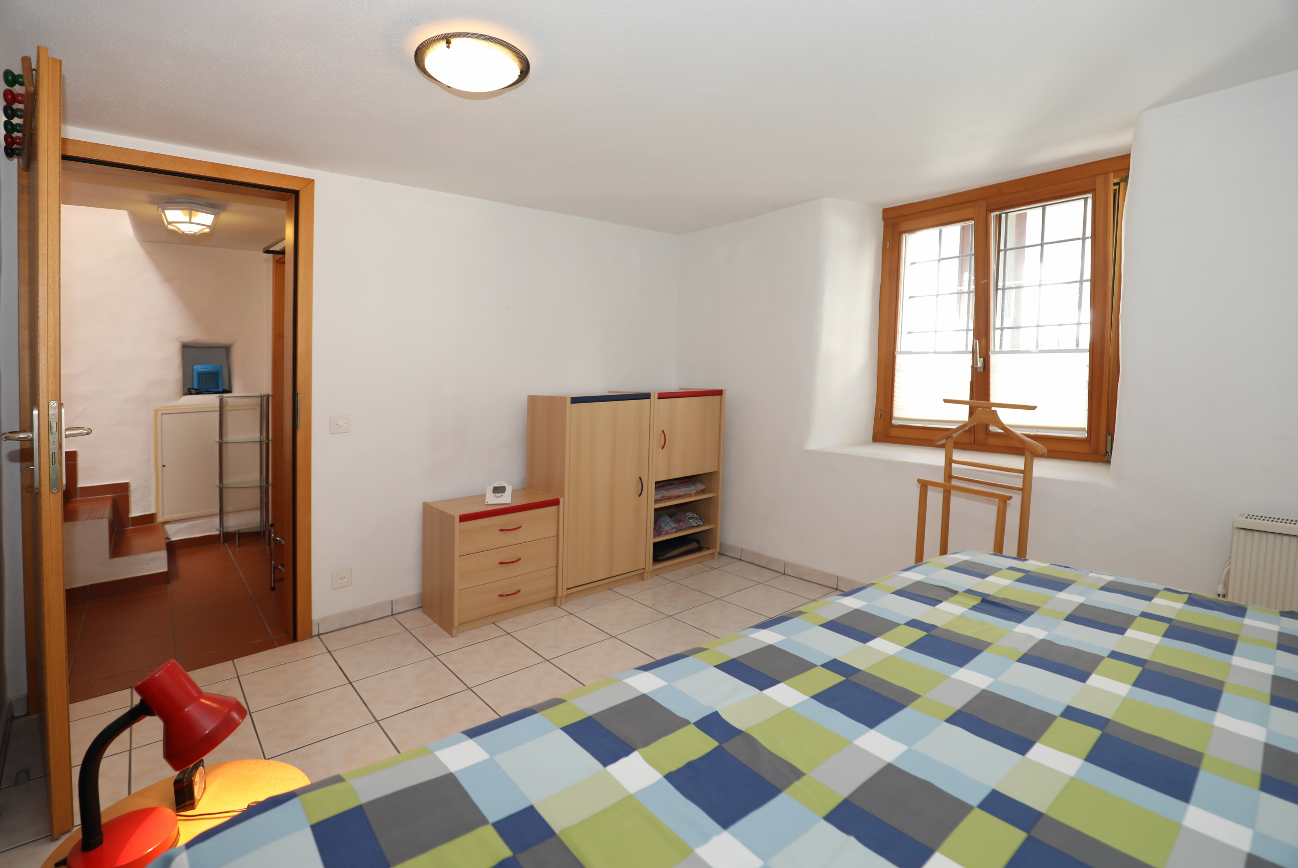 Helles Schlafzimmer mit Fliesenboden und Holzfenstern