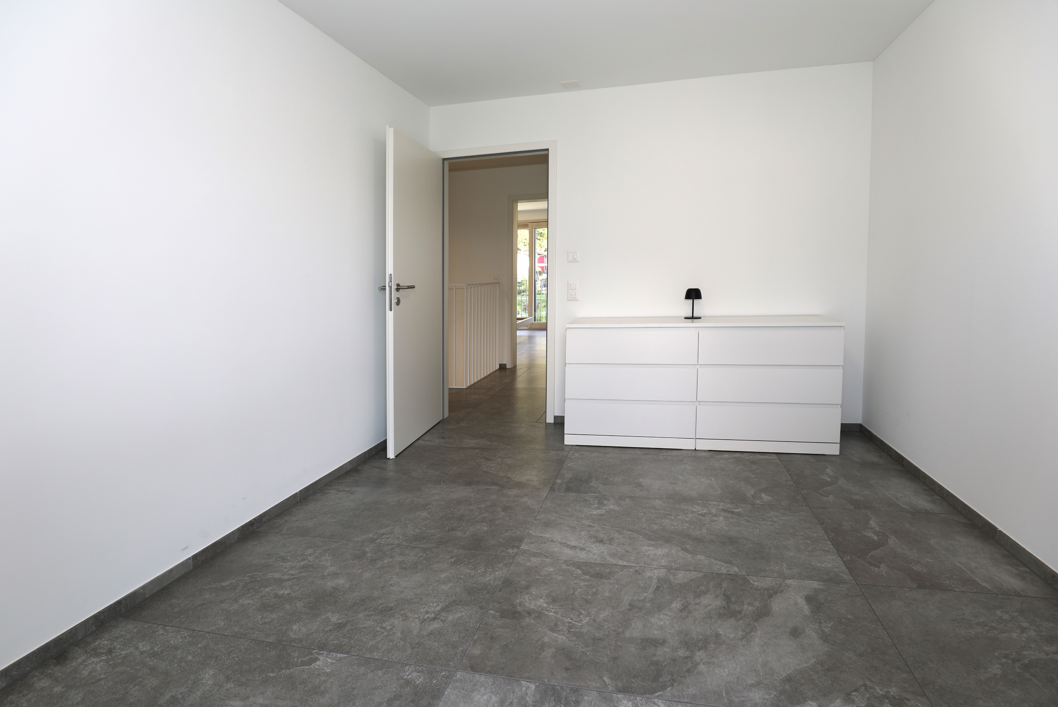 Modernes, leeres Zimmer mit dunklem Fliesenboden und offenem Durchgang