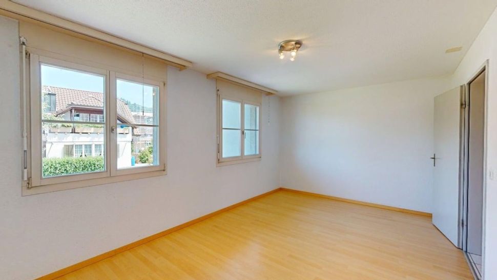 Helles leeres Zimmer mit Parkett und zwei Fenstern