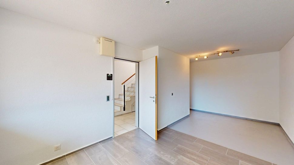 Heller leerer Wohnraum mit offener Tür zum Treppenhaus