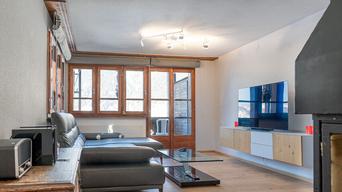 Wohnzimmer mit dunkler Polstergarnitur und TV-Wand