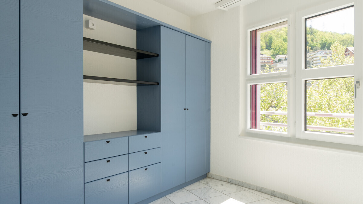 Heller Raum mit blauem Einbauschrank und Fensterblick