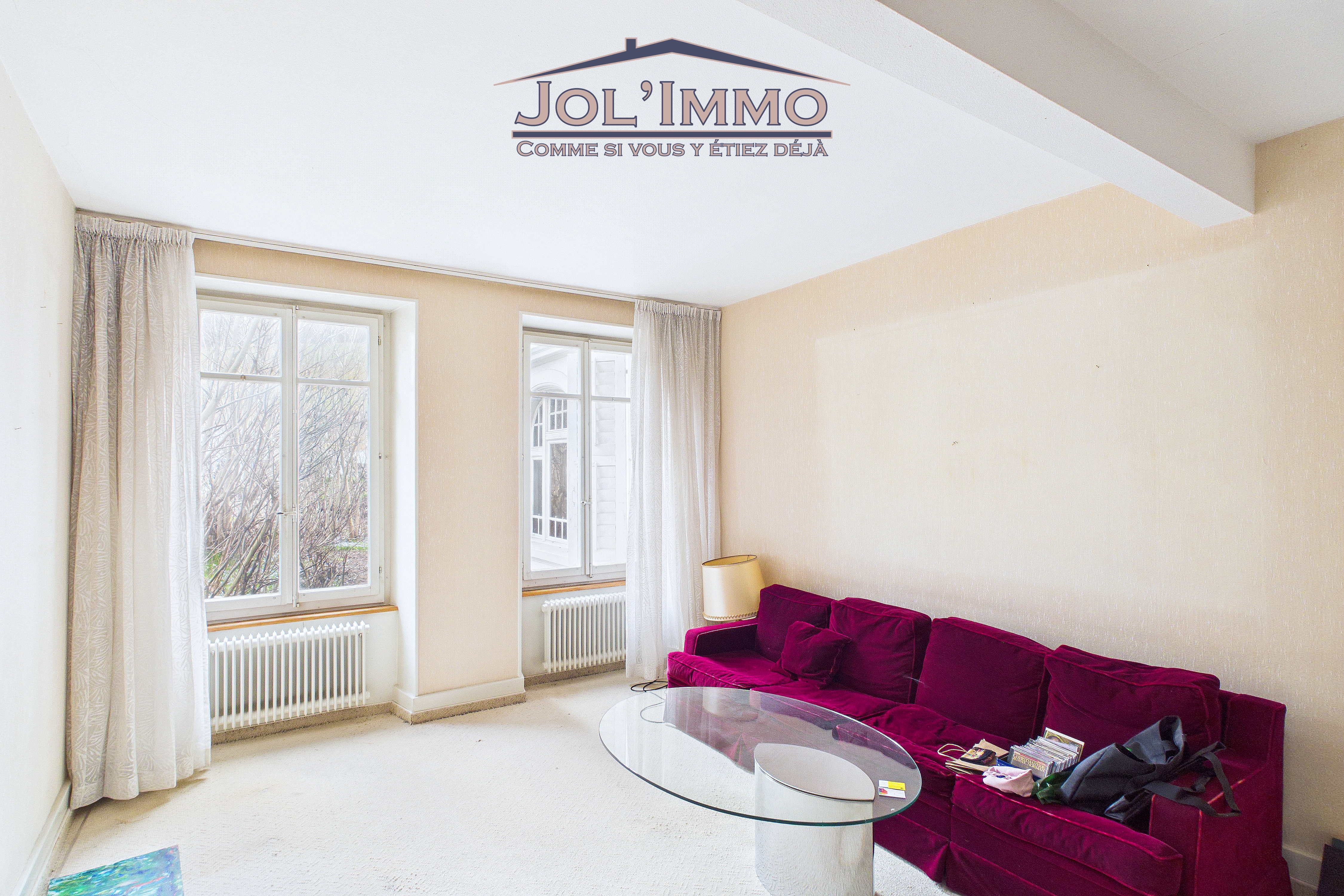 Helles Wohnzimmer mit zwei Fenstern und magentafarbenem Sofa