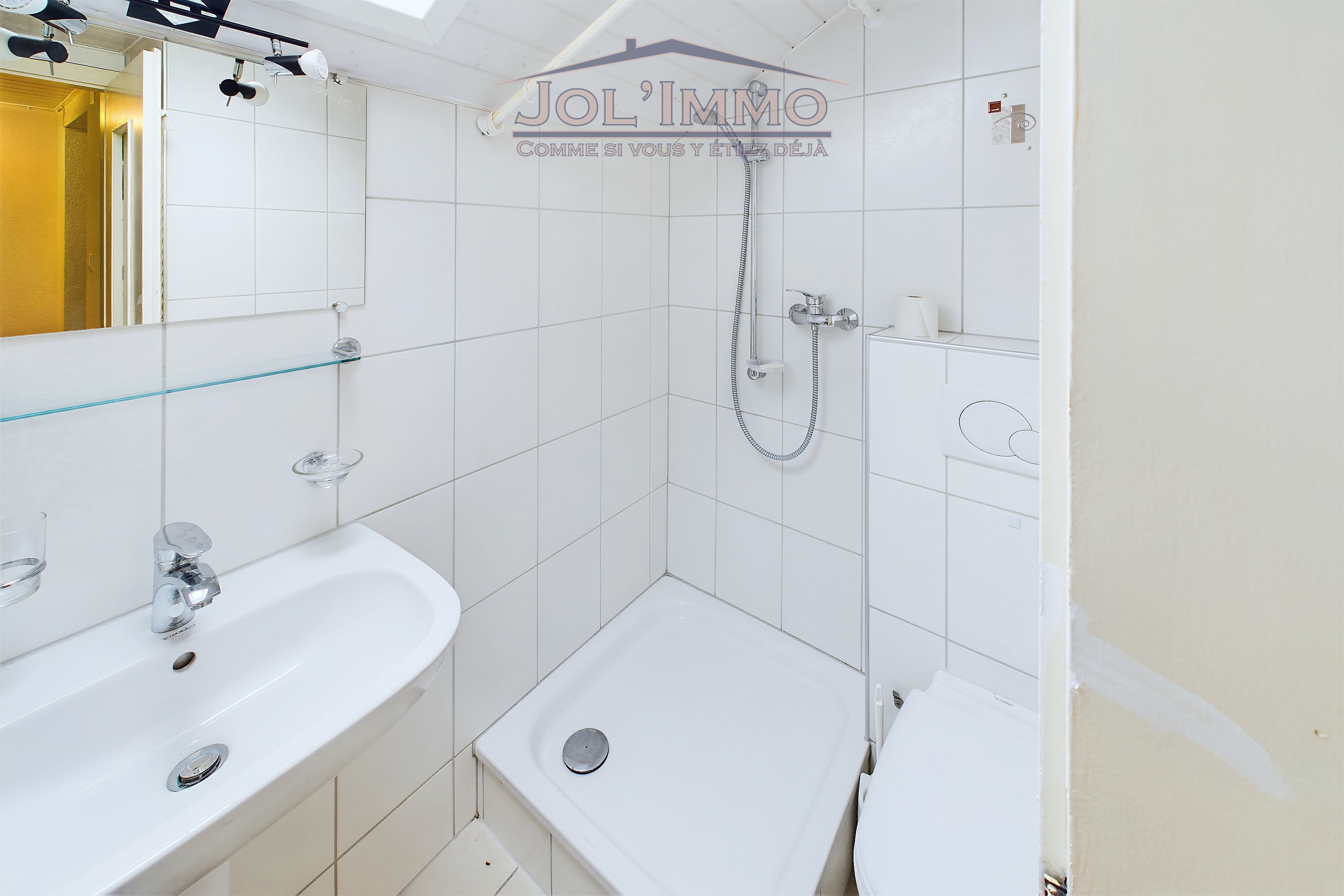 Kleines weiß gefliestes Bad mit Dusche und Waschbecken