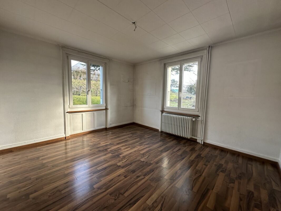 Heller leerer Wohnraum mit Holzoptik-Boden und zwei Fenstern