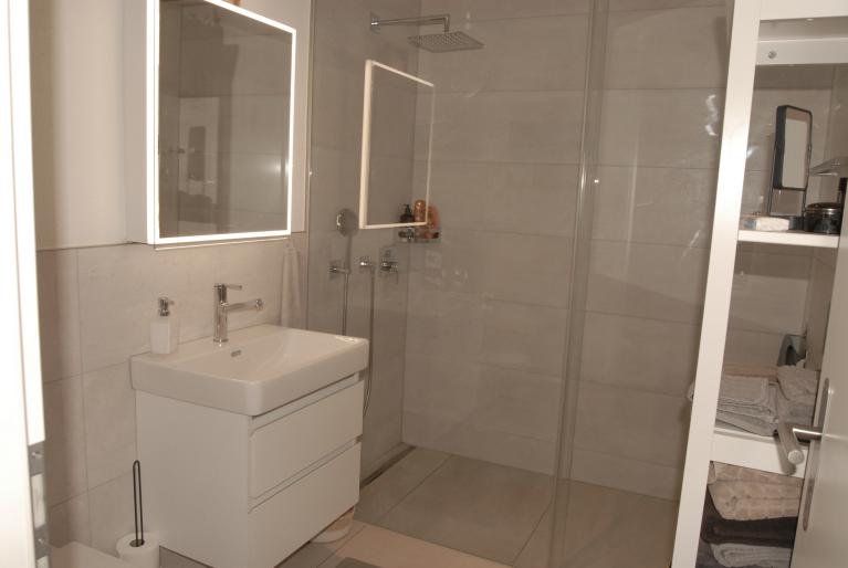Modernes Badezimmer mit begehbarer Dusche und beleuchtetem Spiegel