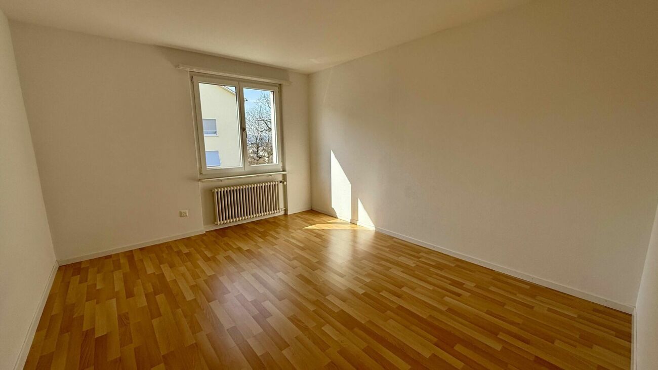 Helles, leeres Zimmer mit Parkettboden und Fenster