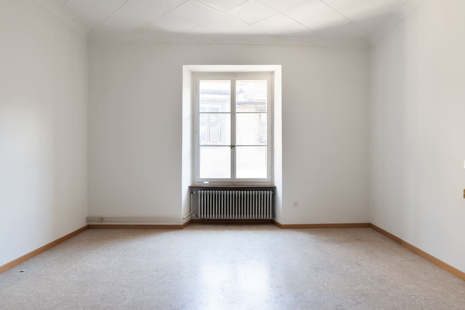 Leerer, heller Raum mit Fenster und Heizkörper