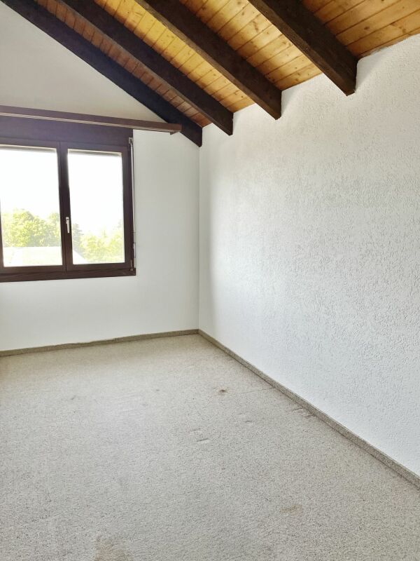 Dachgeschossraum mit sichtbaren Holzbalken und Fenster