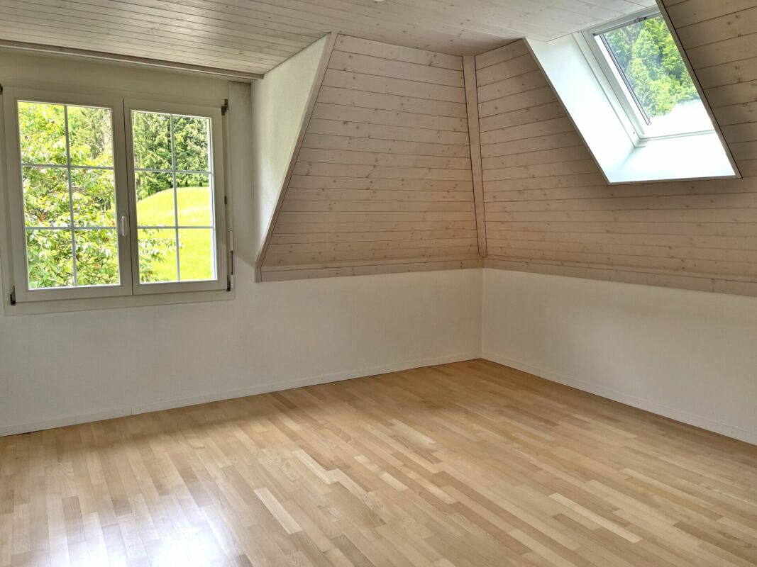 Heller Dachraum mit Holzverkleidung und Fensterblick ins Grüne