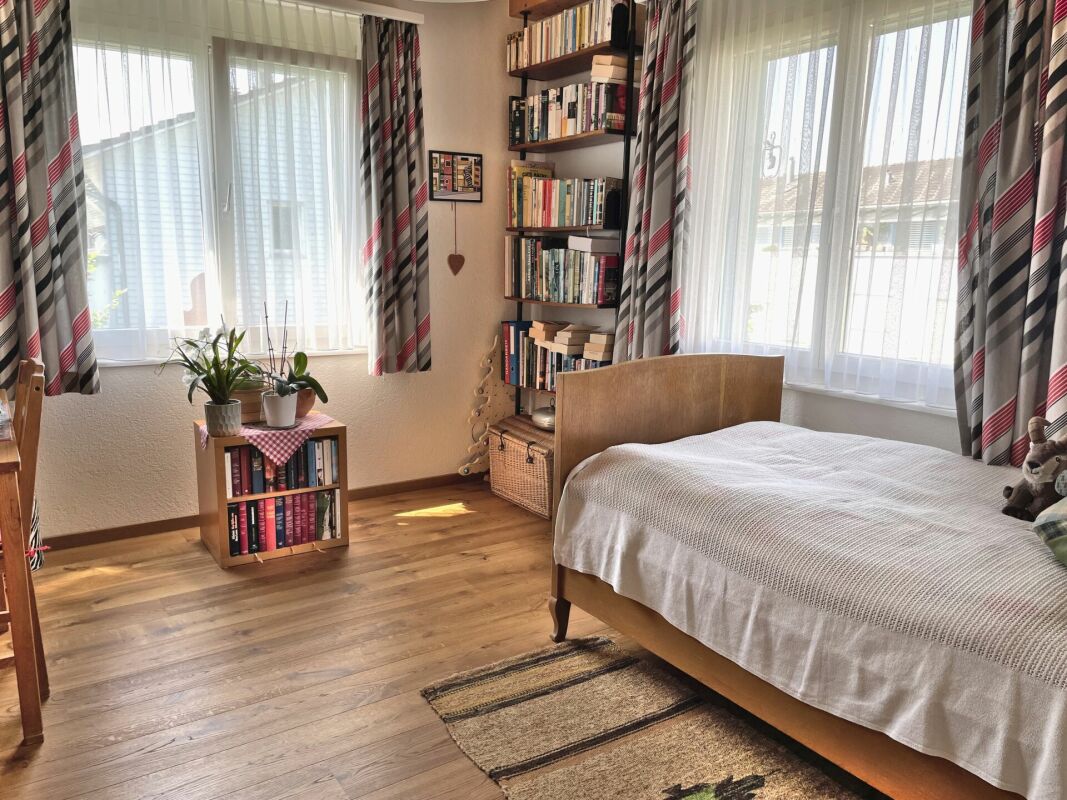 Gemütliches Schlafzimmer mit zwei Fenstern und Bücherregalen