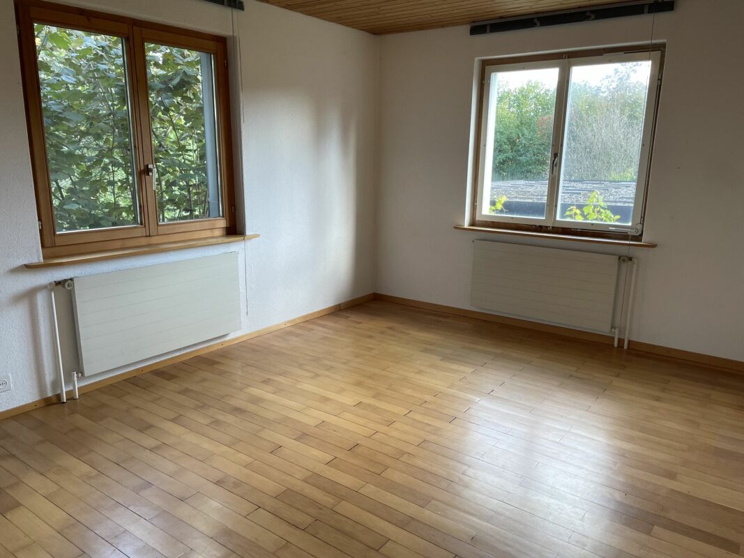 Heller leerer Wohnraum mit Holzfenstern und Parkettboden