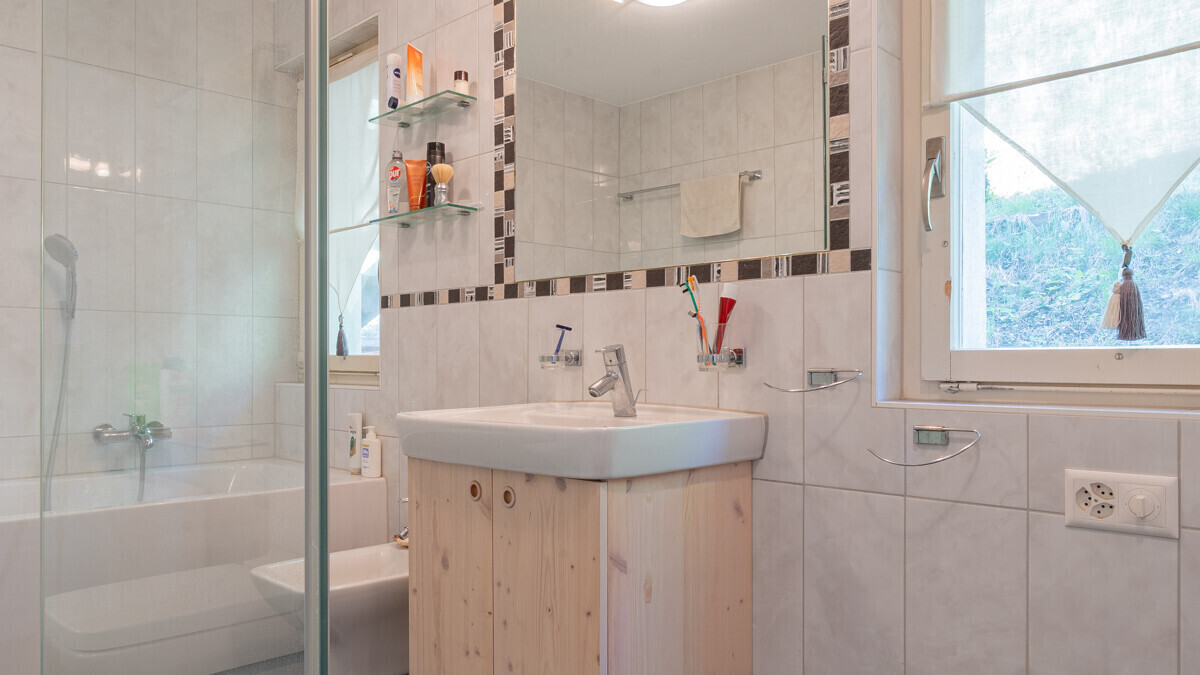 Hell gefliestes Badezimmer mit Badewanne, Waschtisch und Fenster