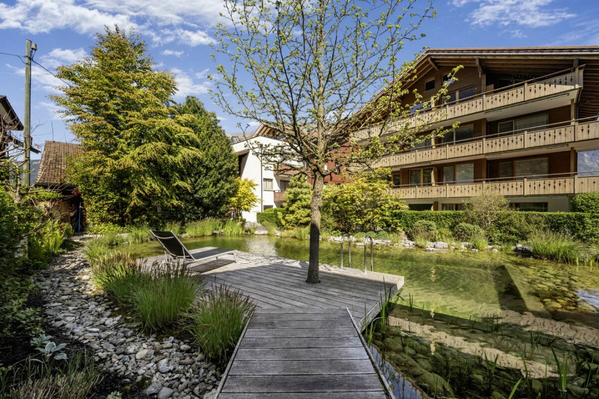 Garten mit Teich und Holzsteg vor alpinem Wohnhaus