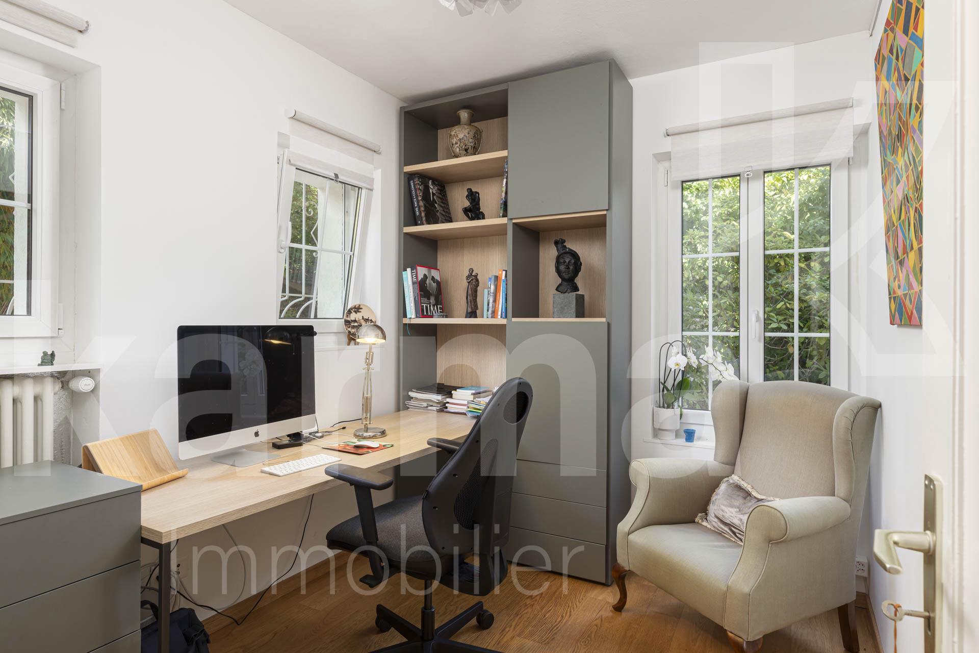 Helles Arbeitszimmer mit Fensterfront, Regal und Sessel