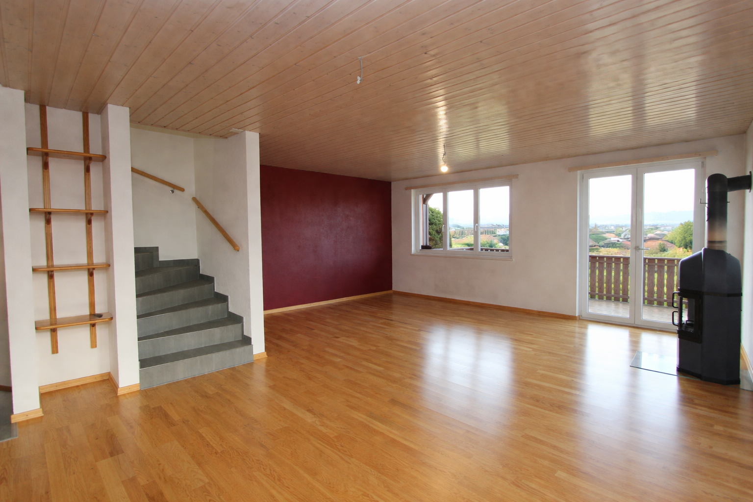 Großer leerer Wohnraum mit Treppe, Holzdecke und Balkonblick
