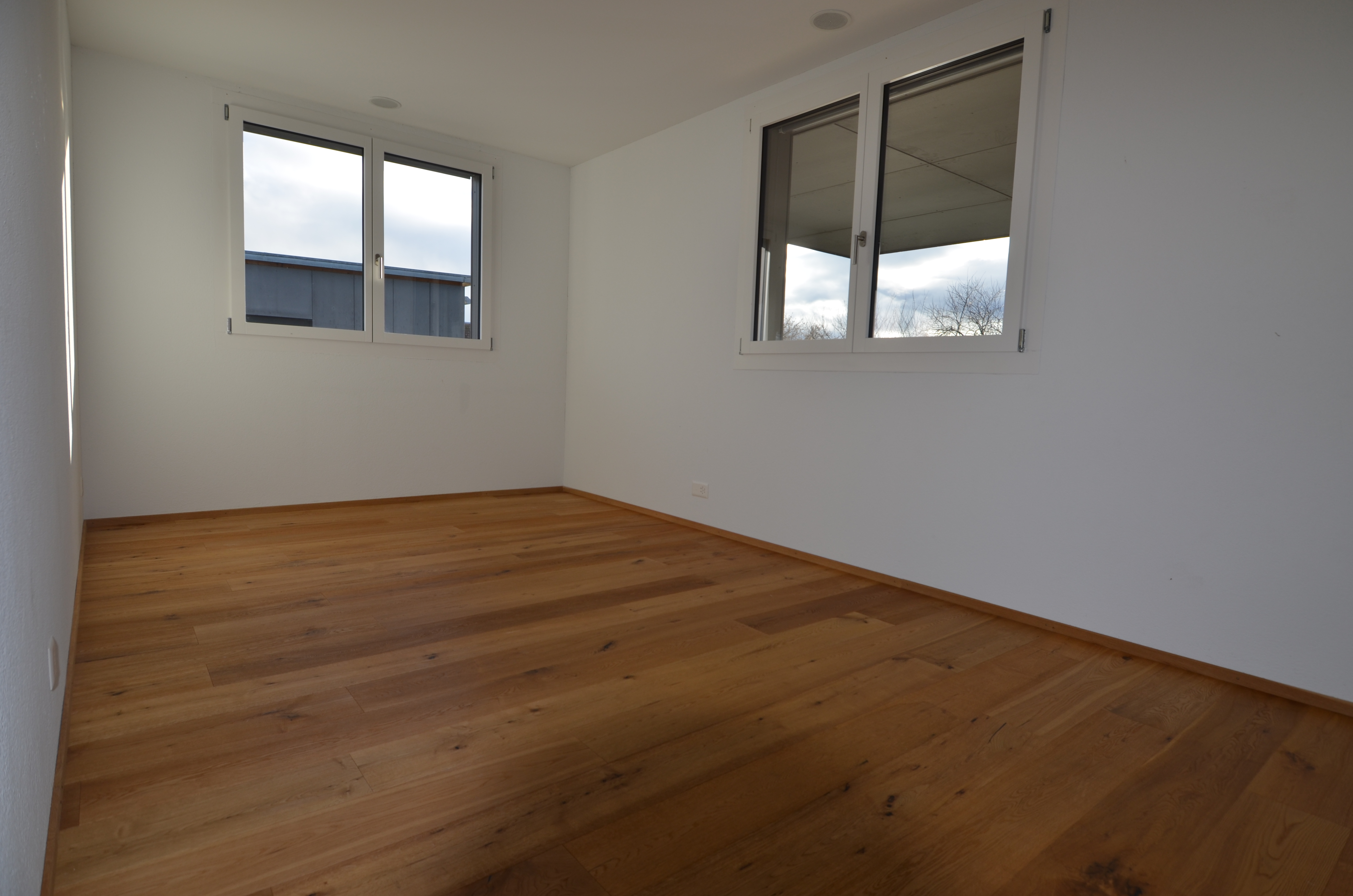 Leerer Raum mit Holzfußboden und zwei Fenstern