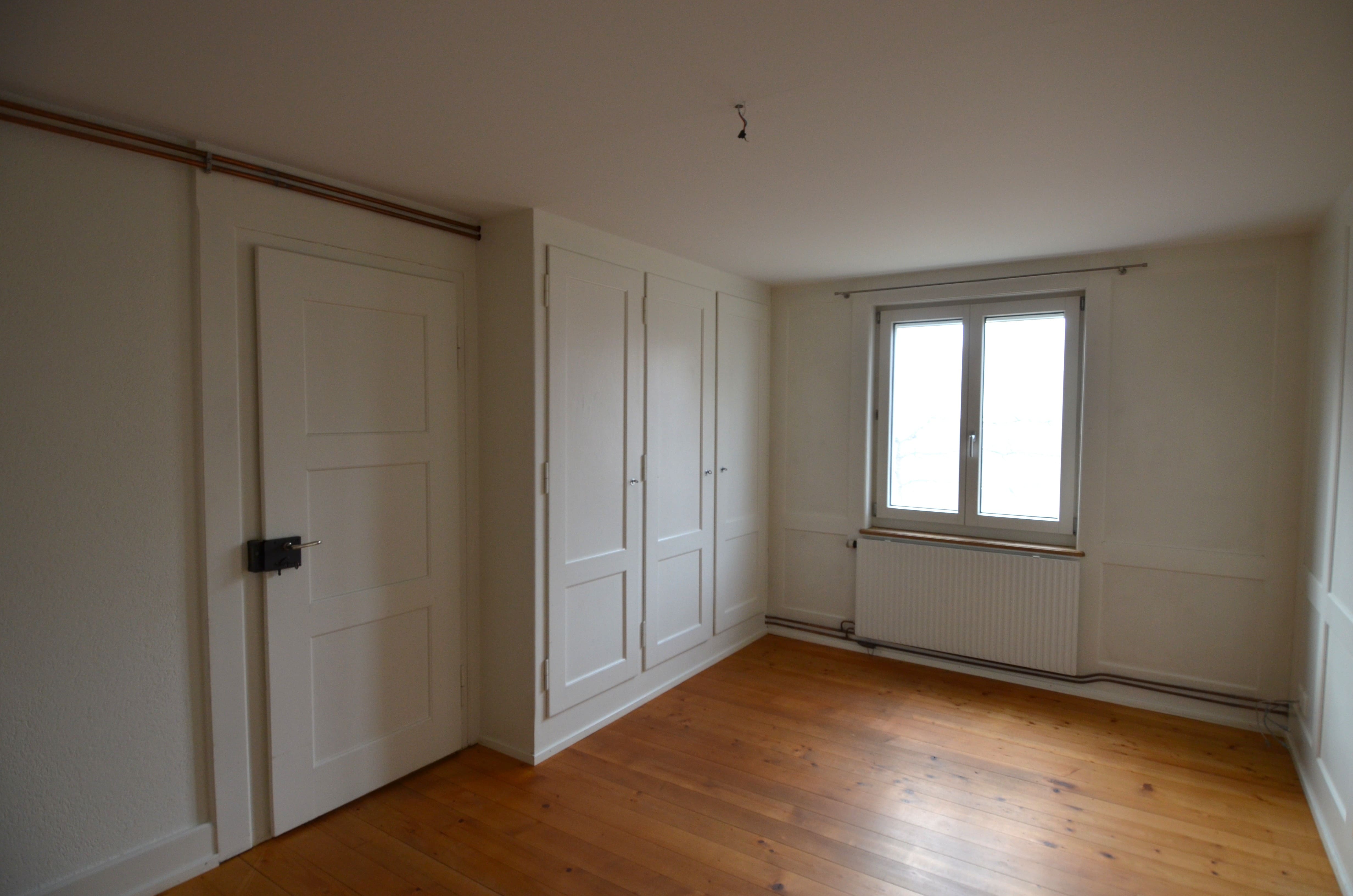 Helles, leeres Zimmer mit Holzfußboden und Einbauschrank