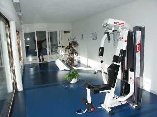 Fitnessraum mit Trainingsgerät und großen Fenstern