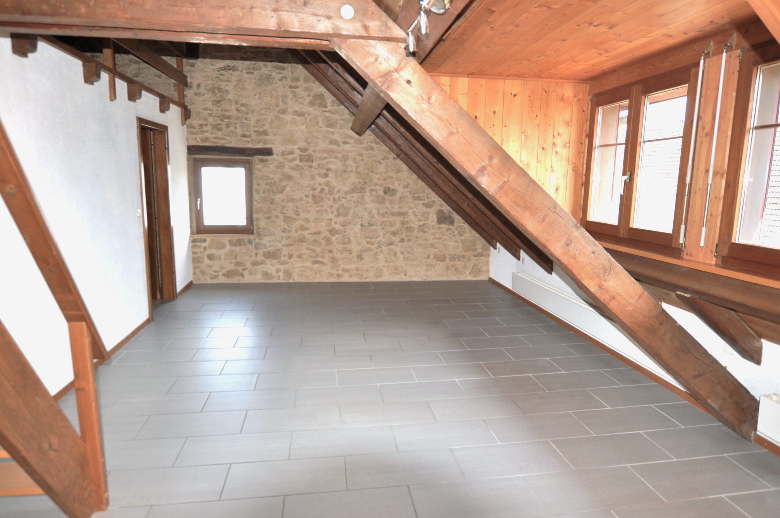 Dachgeschossraum mit Holzbalken und Steinwand