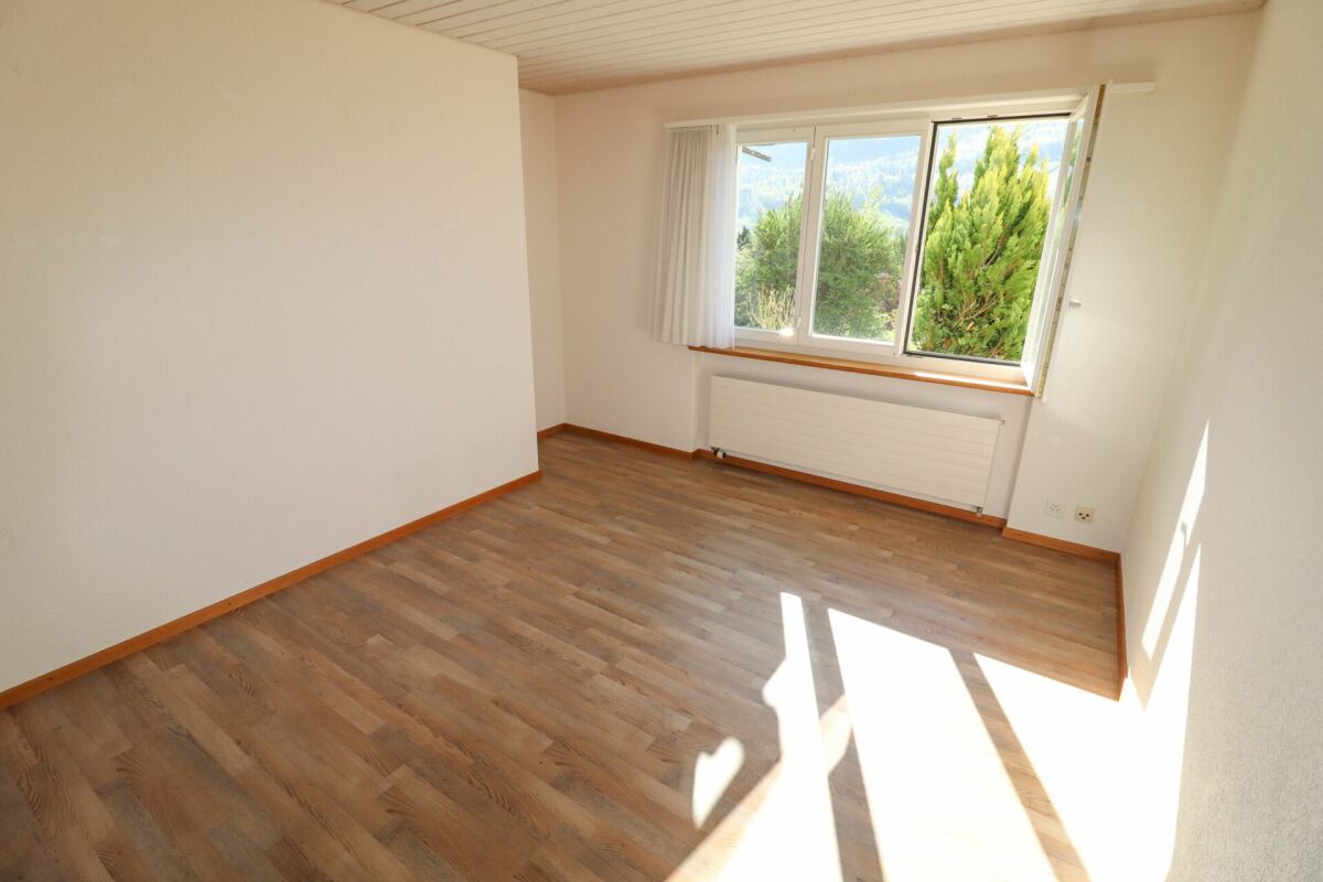 Helles, leeres Zimmer mit Fenster und Holzoptik-Boden