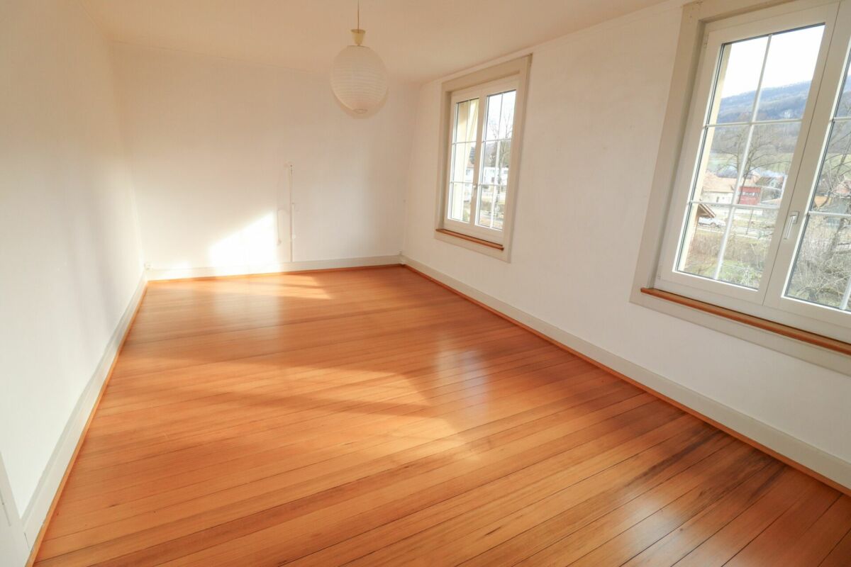 Heller leerer Raum mit Holzfußboden und zwei Fenstern